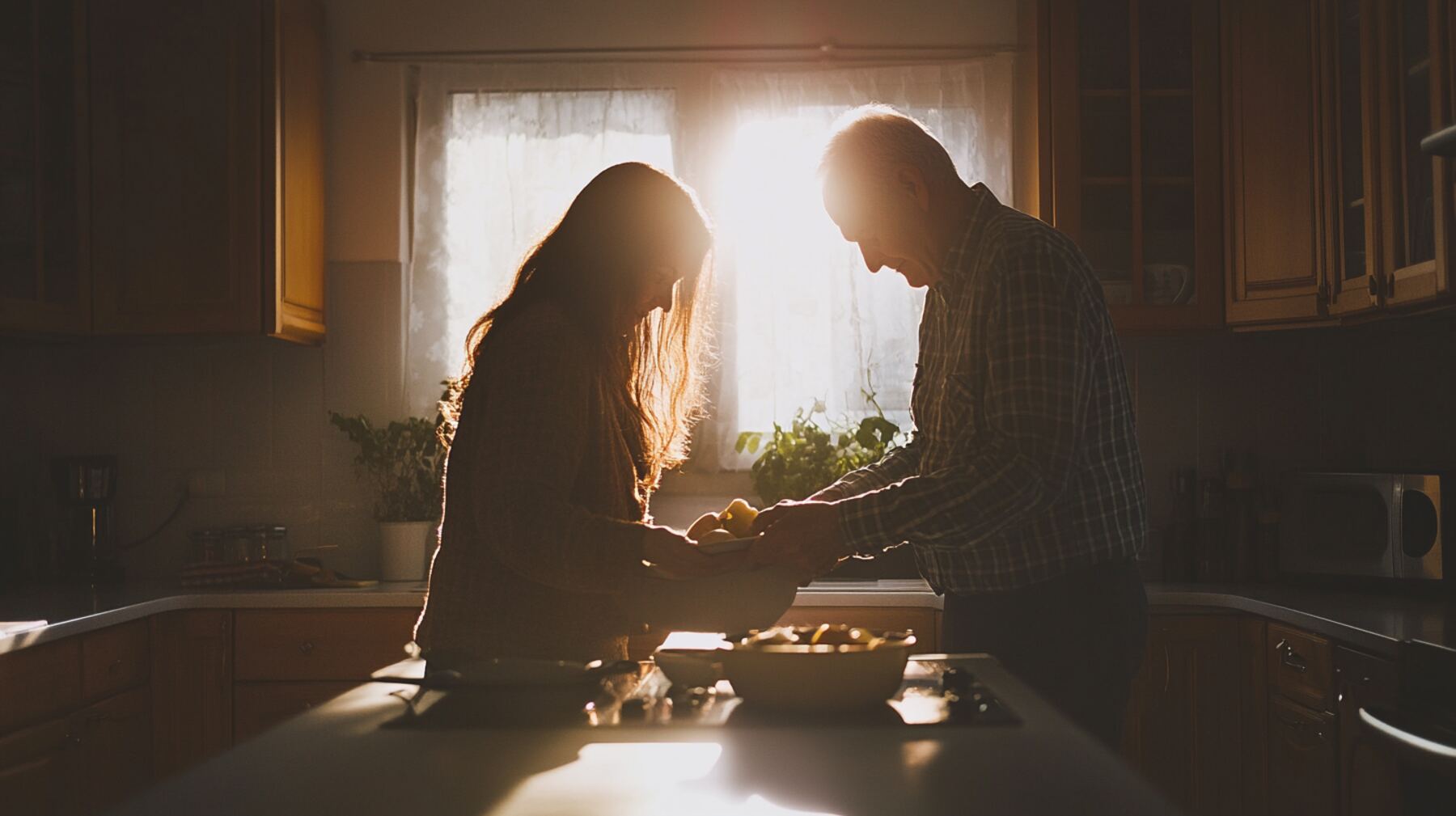An adult daughter and her elderly father cooking together at a sunlit kitchen counter.